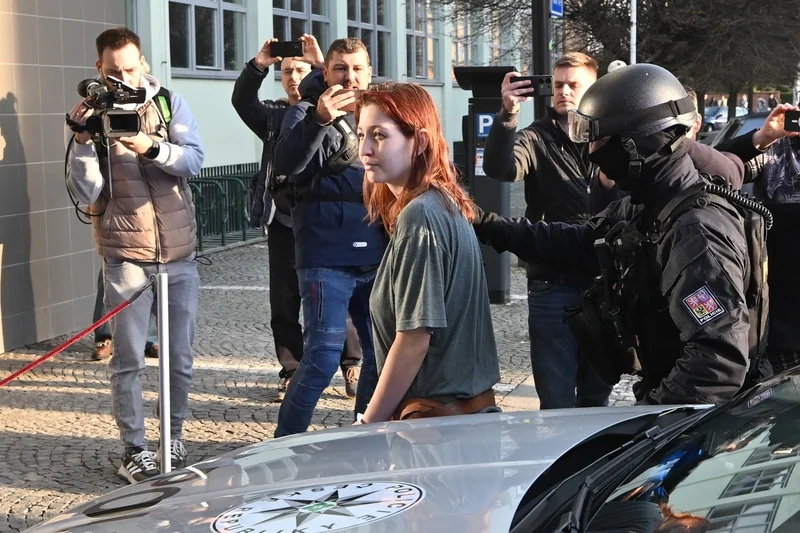 Policisté obviněnou přivádějí k vazebnímu jednání. 